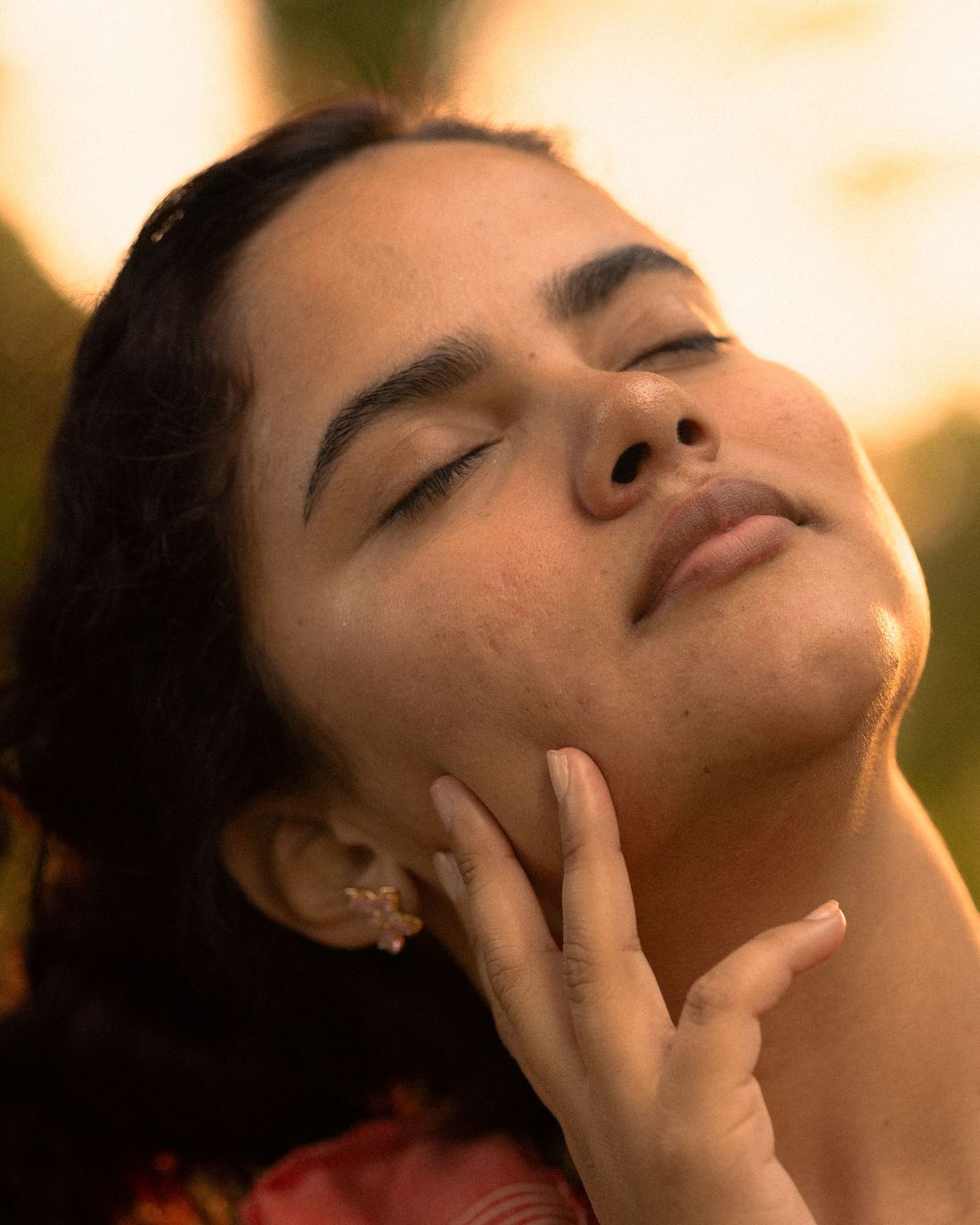 Mulher de olhos fechados, com a pele iluminada pelo sol do fim da tarde